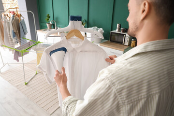 Man steaming clothes with modern steamer in laundry room, closeup