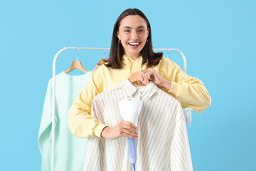 Pretty young woman steaming clothes with modern steamer on blue background