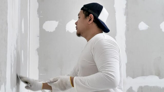 Plasterwork and wall painting preparation. Asian male applying filling drywall patch.
