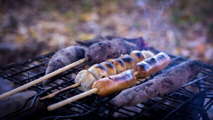 Meatballs, hot dogs, and sweet potatoes are grilled on an iron griddle heated by charcoal. address...