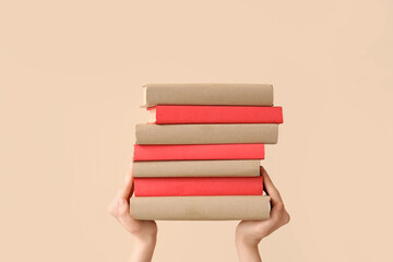 Hands holding stack of books on beige background