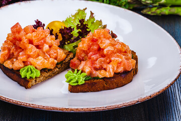 Healthy toasts with rye bread with salmon, avocado mousse, lettuce on white plate.