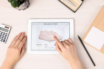 Woman with tablet shopping online at white wooden table, top view