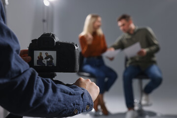 Casting call. Man and woman performing while camera operator filming them against grey background in studio, selective focus - obrazy, fototapety, plakaty