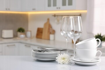 Set of clean dishware, glasses, cutlery and flower on table in kitchen, space for text