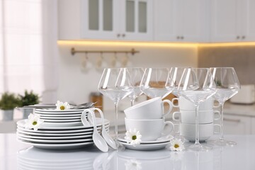 Set of clean dishware, glasses, cutlery and flowers on table in kitchen