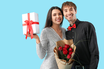 Young couple with bouquet of roses and gift for Valentine's day on blue background