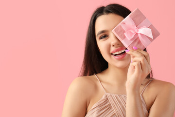 Funny young woman with gift for Valentine's day on pink background