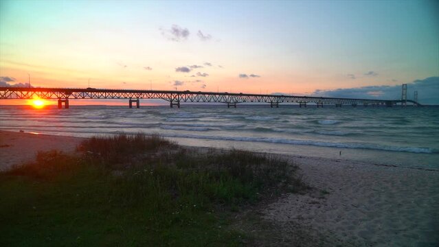 Cinematic aerial landscape Mackinaw Bridge lighthouse Michigan sunset dusk purple pink stunning Great Lakes landscape mid summer up north Petoskey Harbor Springs cars cross bridge birds pan left
