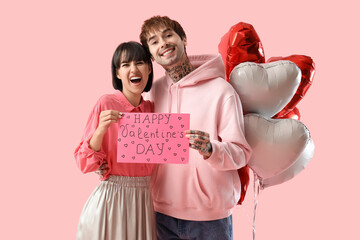 Young couple with heart-shaped air balloons and gift card for Valentine's day on pink background