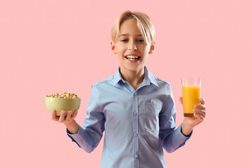 Cute little boy holding glass with orange juice and cereal rings on pink background