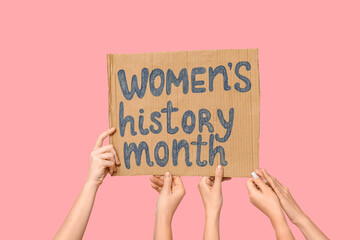 Female hands holding cardboard with text WOMEN'S HISTORY MONTH on pink background