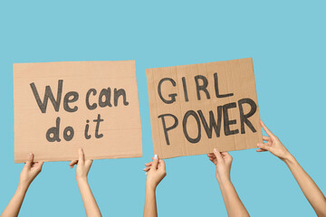 Female hands holding cardboard pieces with text WE CAN DO IT and GIRL POWER on blue background