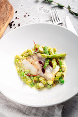 Steamed fillet of white fish with mashed peas and asparagus in a white plate