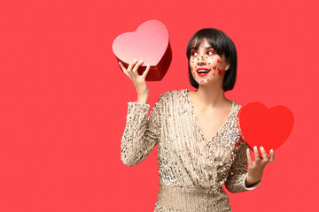 Beautiful young woman with creative makeup and gift boxes for Valentines Day on red background