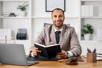 Fototapeta premium Smiling lawyer with book at table in office