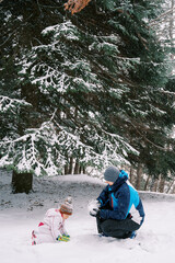 Little girl and dad making snowballs while squatting in a snowy forest