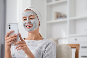Young woman with face mask using smartphone at home, space for text. Spa treatments