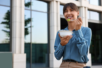 Happy businesswoman with plastic bowl of salad having lunch outdoors