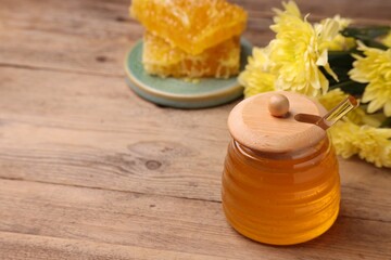 Sweet golden honey in jar and chrysanthemum flowers on wooden table, space for text