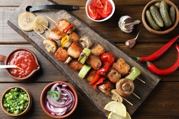 Delicious shish kebabs, mushroom, tomato and zucchini served on wooden table, flat lay