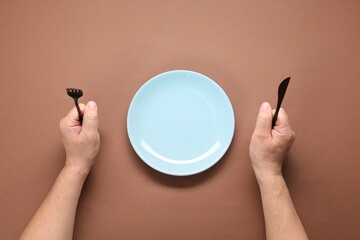 Man with cutlery and empty plate at brown table, top view