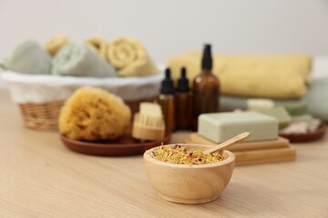 Bowl with dry flowers, soap bar and bottles of essential oils on light wooden table. Spa therapy