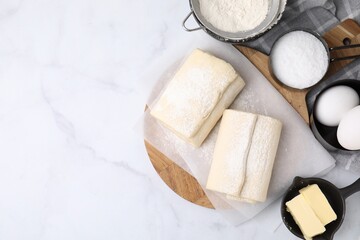 Raw puff pastry dough and ingredients on white marble table, flat lay. Space for text