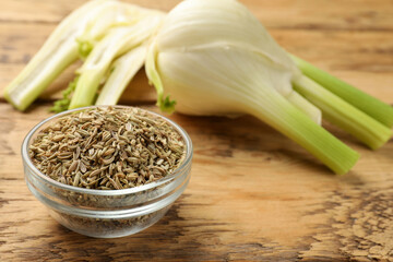 Fennel seeds in bowl and fresh vegetables on wooden table, closeup - obrazy, fototapety, plakaty