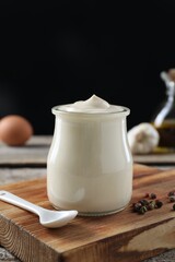Fresh mayonnaise sauce in glass jar on wooden table, closeup