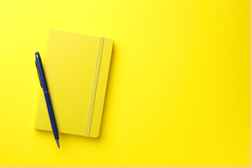 Closed notebook and pen on yellow background, top view. Space for text