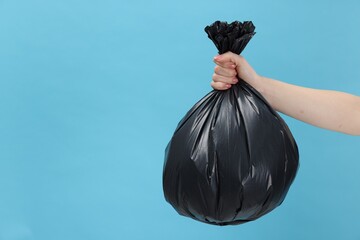 Woman holding plastic bag full of garbage on light blue background, closeup. Space for text