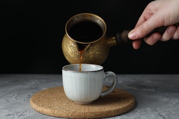 Turkish coffee. Woman pouring brewed beverage from cezve into cup at grey table, closeup