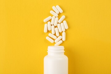 Bottle and vitamin capsules on yellow background, top view - obrazy, fototapety, plakaty