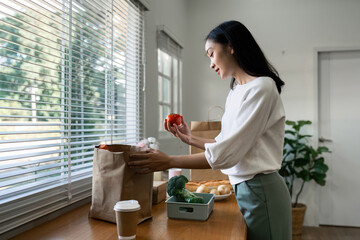 Organic Food Delivery. Happy young woman unpacking bag with Fresh Vegetables in kitchen