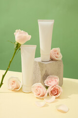 Obraz na płótnie Canvas Close-up of two unlabeled cosmetic tubes displayed with fresh roses and a stone platform. Beige surface with pastel green background. Blank label for design.
