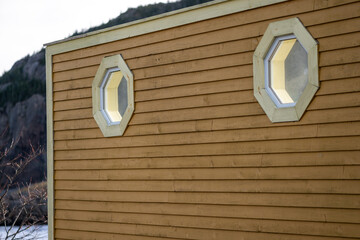 The outside exterior wall of a yellow-mustard color wooden clapboard wall with two glass octagon...