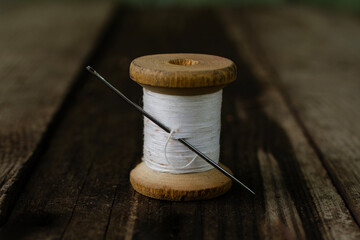 a bobbin with white thread and a needle with black thread stuck into it stands on a wooden table. closeup thread for sewing and needlework, old reel of thread