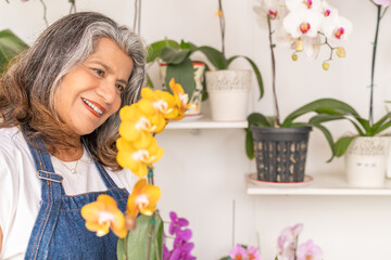 Smiling woman observing a yellow orchid inside the house