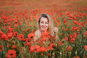 Happy woman in a red dress in a beautiful large poppy field. Blond sits in a red dress, posing on a large field of red poppies