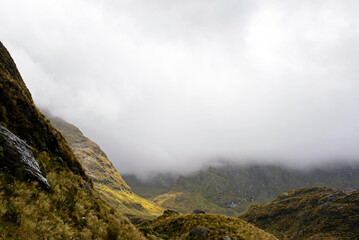 Summit of the Routeburn mountain trail with rocks and vegetation in the clouds, New Zealand
