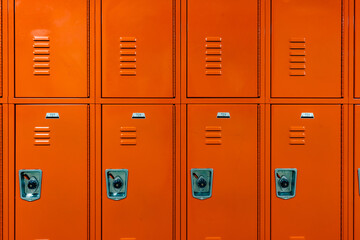 Orange metal lockers along a nondescript hallway in a typical US High School.  No identifiable information included and nobody in the hall.	