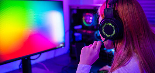 Happy Gamer endeavor plays online video games tournament with computer neon lights, young woman wearing gaming headphones intend to do playing live stream games online at home - obrazy, fototapety, plakaty