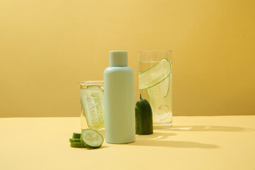 An unlabeled bottle and two glasses of cucumber detox water on a minimalist background. The abundant Vitamin C in cucumbers will stimulate new skin growth.