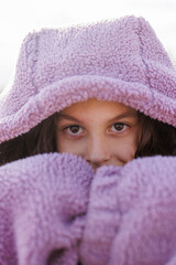 portrait of a boy in a purple sweater with the hood pulled low over his eyes. A child in a warm jacket.