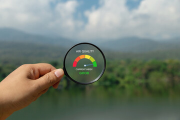 Good air quality outdoors. Hand holding a magnifying glass to check the good air quality at the green level safe from pollution dust PM 2.5.good air quality at beautiful summer landscape. AQI - obrazy, fototapety, plakaty