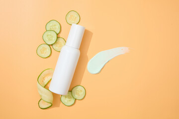 Cucumber slices, a white cosmetic bottle and a splash of texture displayed on a minimalist pastel background. Copy space with view from above.
