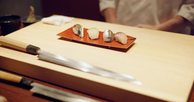 Hands, sushi plate and presentation in restaurant on table at diner, cuisine or expert cooking in night. Person, kitchen or fish with catering, ready and service for nutrition, diet or snack in Japan
