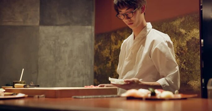 Sushi chef, cloth and table in kitchen for cleaning, food or hygiene at diner, cuisine or cooking in night. Person, man and fabric at restaurant, store and stop bacteria for nutrition, diet or health
