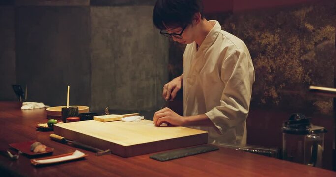 Sushi, fish and chef at restaurant cooking on table at diner or cuisine with ingredients at night. Kitchen, knife and culinary artist preparing a gourmet Japanese food, meal or snack at catering job.